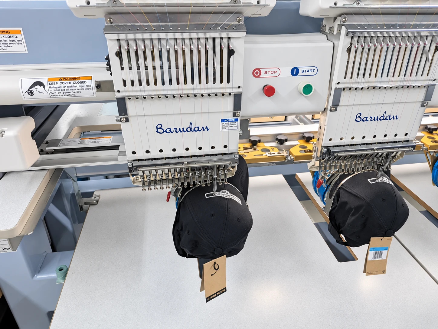 Edited photo: Close view of black caps mounted beneath Del Print’s embroidery machine heads