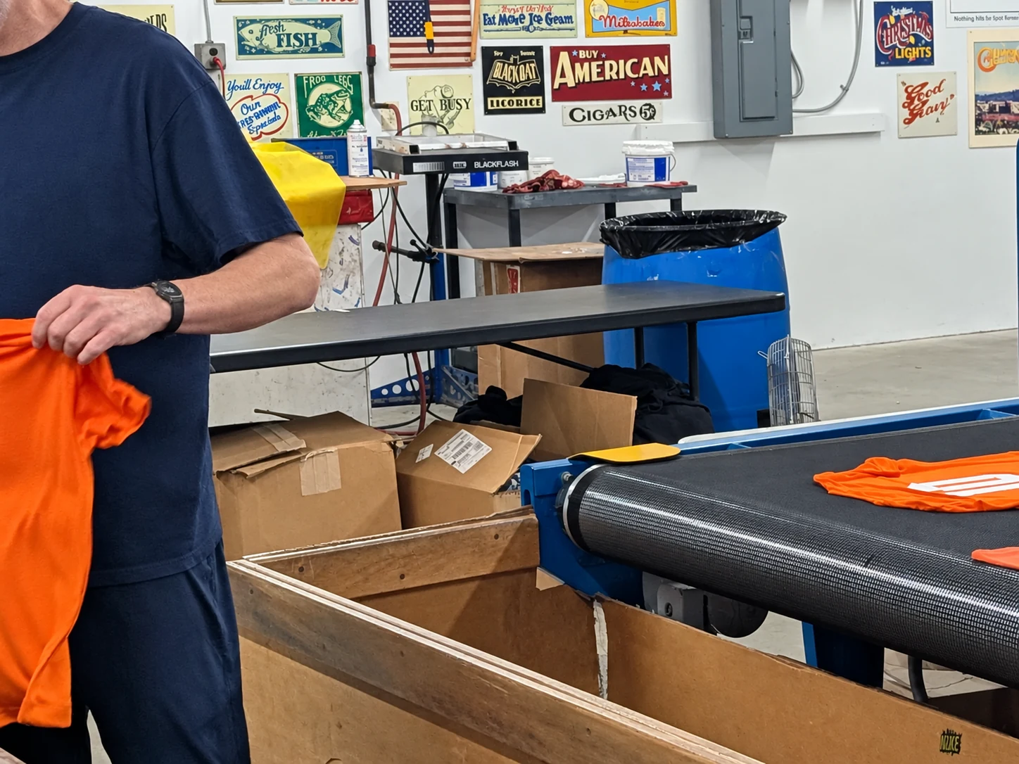 Edited photo: A Del Print employee handling orange shirts beside the drying conveyor