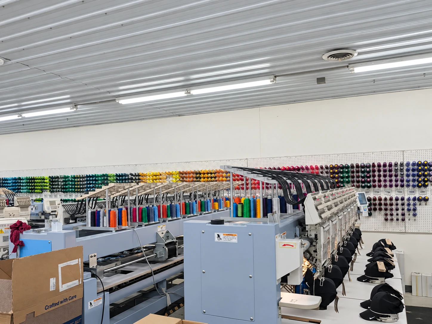 Edited photo: A row of embroidery machines with colored thread along the wall at Del Print