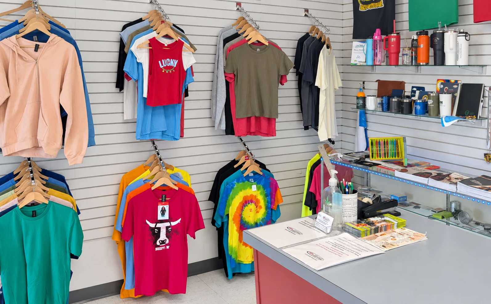 Edited photo: Printed tees, embroidered shirt samples, and drinkware displayed in Del Print’s showroom