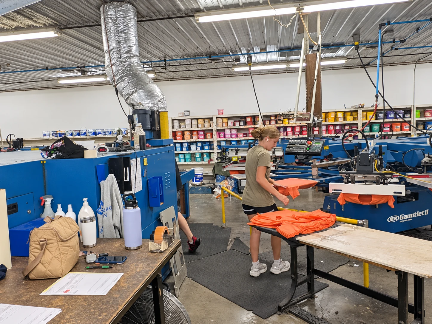 Edited photo: A Del Print employee loading orange garments onto a screen printing press